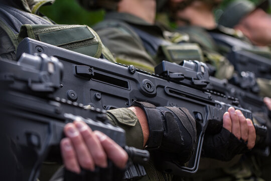Close up side view of a row of soldiers in green gear holding modern black bullpup assault rifles with red dot collimator sights ready for dangerous military combat defense war operation