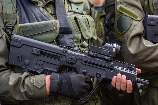 Close up view of a soldier in green tactical gear holding a modern black bullpup assault rifle with a red dot collimator sight ready for dangerous battle combat defense war action outdoors