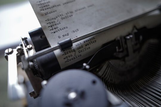 Old vintage black typewriter with a typed menu dated May 8 1945 stands on a wooden table near a retro camera in a military field camp creating a unique historical World War II atmosphere