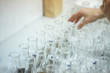 Scientist hand arranges glass Erlenmeyer flasks with dry soil samples on the white table preparing for chemical analysis research in the modern agricultural laboratory center indoors