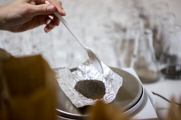 Close up view of a scientist hand adding dry soil powder sample on the aluminum foil on the electronic balance scale for chemical agrochemical analysis research in the laboratory