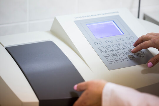 Close up view of a scientist hand pressing buttons on the control panel of a modern UV VIS double beam spectrophotometer device during chemical research analysis in the laboratory room