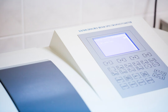 Close up view of a scientist hand pressing buttons on the control panel of a modern UV VIS double beam spectrophotometer device during chemical research analysis in the laboratory room