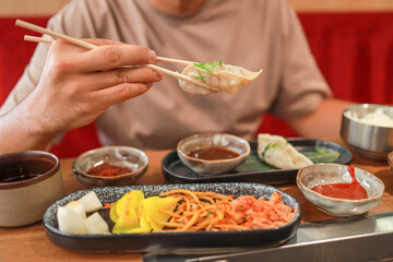 A man holds a traditional Korean steamed dumpling on chopsticks at a Korean restaurant. Asian food. Global food culture