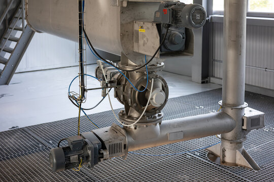 An automated industrial system for conveying bulk powder in a modern factory. A screw conveyor (auger) feeds material to a rotary valve (airlock) installed under a large stainless steel hopper.