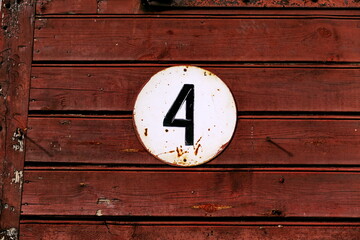 Numéro 4. Plaque émaillée de numéro de rue sur mur de bois marron.