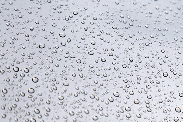 Dense Raindrops on a Window – Natural Water Texture,A detailed macro photograph of numerous raindrops scattered across a glass window with a soft gray backdrop. The image emphasizes the 