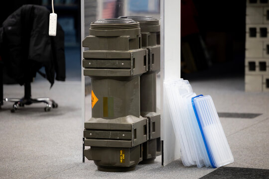 An olive-green military transport container for anti-tank missile. The weapon case stands on the carpeted floor of an office, next to plastic storage bins.