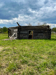 Abandoned wooden cabin structure in a grassy field under a cloudy sky, showcasing rustic architecture and natural surrounding, highlighting the beauty of decay and the passage of time in nature