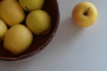 Yellow apples filling a rustic brown bowl and a single apple resting alongside, creating a fresh, healthy still life on a speckled white kitchen countertop, representing wholesome nutrition
