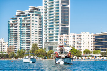 Two boats floating on water with modern apartment buildings in the background in Limassol, Cyprus