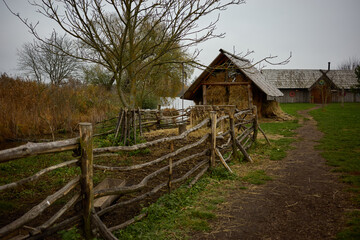 Rustic farm landscape with straw shed and wooden fence beside a calm waterway in early spring