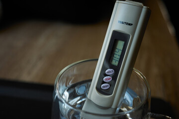 Portable water quality analyzer (salt meter) that measures the total amount of substances dissolved in water of water in a glass during a kitchen experiment at home in the morning