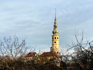 Obraz premium Tovacov Castle, located in the Czech Republic, features a prominent tower with a distinctive onion-shaped dome and vertical spire. The structure is surrounded by leafless trees, indicating a winter 