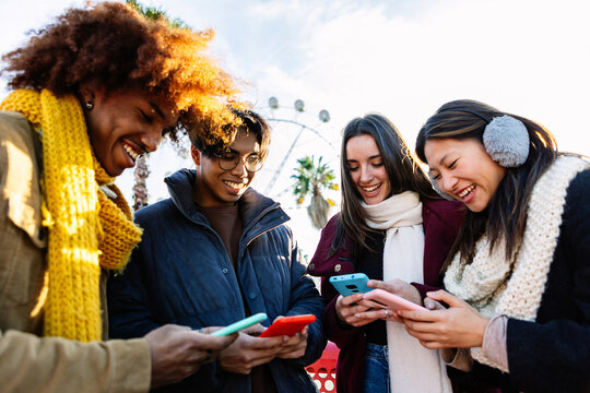 Young group of people in warm clothes using mobile phone device on winter. Social media and technology lifestyle concept
