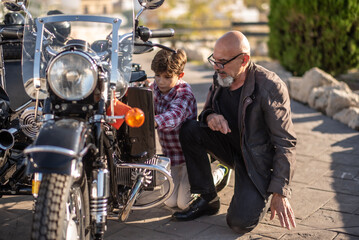 Grandfather and grandson: The 60-year-old man shows his grandson the motorcycle and they adjust it.