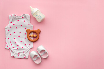 Baby bodysuit with wooden teethers and bottle of milk on pastel pink background, top view