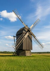 Fototapeta premium Rustic Wooden Windmill in Summer Field - An old wooden windmill stands tall in a green field under a blue sky. Symbolizes heritage, sustainability, countryside, architecture, and tradition