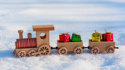 A wooden toy train with presents in the snow. A Christmas locomotive with carriages loaded with brightly colored boxes.