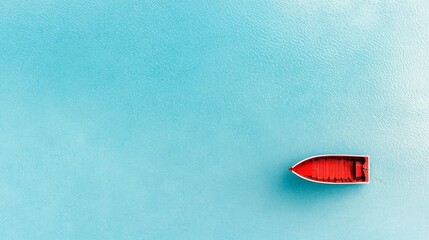 An overhead aerial view shows a solitary red rowboat adrift on a tranquil, bright turquoise body of water.