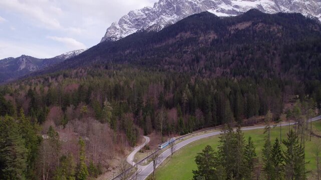 High Quality aerial view of the Zugspitze region with the iconic Zahnradbahn cutting through the forest framed by alpine peaks soft light crisp air and a calm cinematic feel.