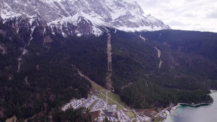 High Quality aerial view of the Zugspitze with snow covered peaks dense forest below and the cable car gliding up the mountain suspended in bright alpine light atmosphere steady and calm.