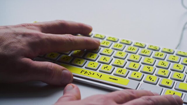 Close up hand of a blind person reading some braille text on keyboard to learn. Finger of blind student touching the braille alphabet. Disabled person concept. Palms moving tactile keys, creating text
