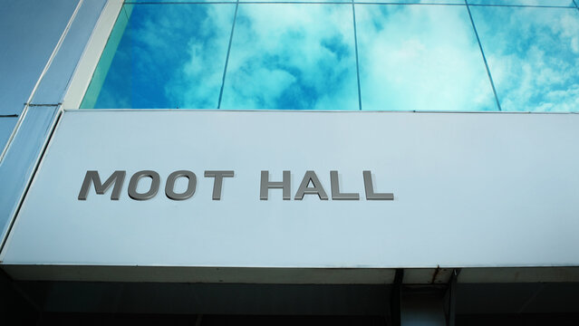 Moot Hall sign displayed on a modern glass building with windows reflecting clouds and sky, creating a clean, bright, contemporary exterior with civic atmosphere