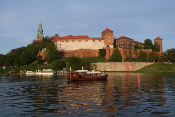 Naklejka premium Historic Wawel Castle complex and Vistula River with cruise ship in foreground in afternoon sunlight. Krakow, Poland