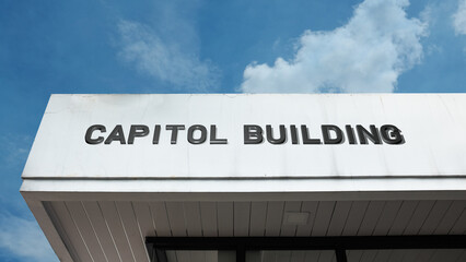 Obraz premium Capitol Building word sign displayed on a building under a clear blue sky, representing government, legislative work, civic administration, and political institutions