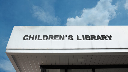 Obraz premium Children’s Library word sign displayed on a building under a clear blue sky, representing reading, education, learning, literacy, books, and community knowledge resources