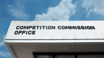 Obraz premium Competition Commission Office word sign displayed on a building under a clear blue sky, representing regulatory authority, business oversight, government services, and administration