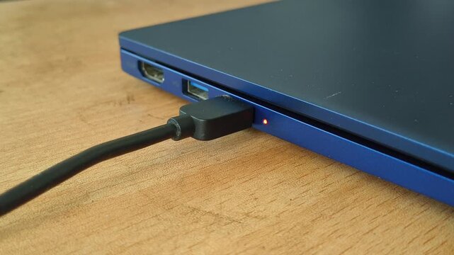 Hand plugging or connecting a usb type c black charger power cable cord into a laptop device charging port hole with glowing led light. Electricity or energy concept. Close up side view.