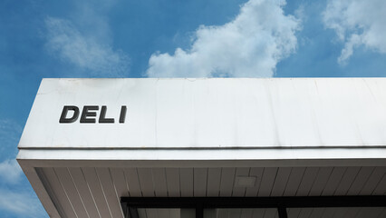 Deli word sign on a building under a clear blue sky, representing a food establishment, fresh produce, sandwiches, deli meats, cuisine, and local dining options