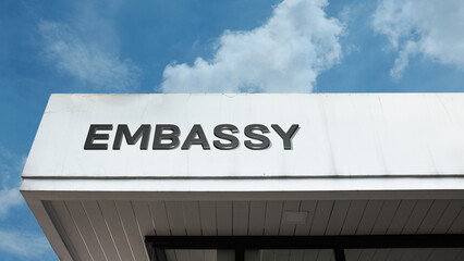 Embassy sign displayed on a building against a clear blue sky, symbolizing diplomacy, international relations, foreign affairs, governmental authority, and political representation