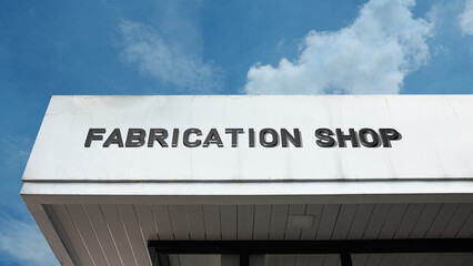 Fototapeta premium Fabrication Shop sign displayed on a building against a clear blue sky, symbolizing manufacturing, custom assembly, industrial workshop, metalwork, and specialized production