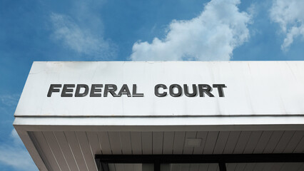 Federal Court sign displayed on a building against a clear blue sky, symbolizing judicial system, national law, governmental authority, justice, legal proceedings, and civil rights
