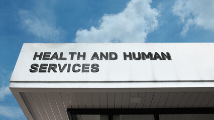 Health and Human Services sign displayed on a building against a clear blue sky, symbolizing public welfare, social support, medical aid, and civic aid