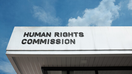 Human Rights Commission sign prominently displayed on an official building exterior, set against a clear blue sky, symbolizing justice, advocacy, and legal protection