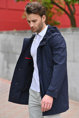 A man in a navy jacket adjusts the front of his coat while standing outdoors. Soft lighting and neutral tones emphasize a clean, stylish everyday look.