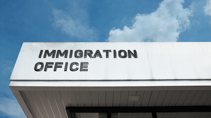 Obraz premium Immigration Office sign on a building against a clear blue sky, symbolizing government agency, border control, visa services, and policy