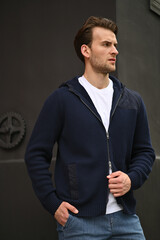 A man in a dark hoodie stands against a shadowy urban wall. Strong contrast and a clean pose create a moody contemporary portrait.