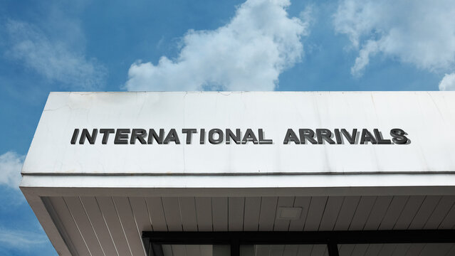 International Arrivals sign on a building against a clear blue sky, symbolizing air travel, customs, border crossing, passenger entry, and greeting