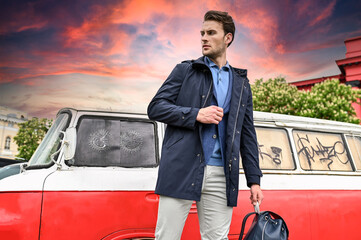 A man in a blue jacket stands against a dramatic sunset sky and a retro van. Warm tones and soft cinematic light create a travel-inspired atmosphere.