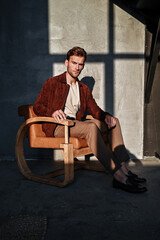 A man in a green T-shirt poses against a concrete wall, standing casually with one knee bent. The raw texture of the background adds a bold, contemporary fashion edge.