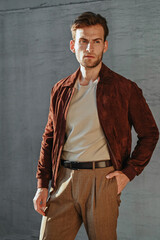 A man sits comfortably with one arm resting on the chair, wearing a fitted green T-shirt and light trousers. Clean lighting highlights his athletic build and stylish casual aesthetic.