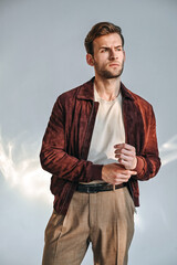 A warm portrait of a man in a suede jacket, adjusting the collar with subtle confidence. Natural light emphasizes his features and the texture of the outfit, giving a refined editorial feel.