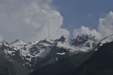 Obraz premium Snow-capped mountain peaks under blue sky with fluffy clouds in the afternoon