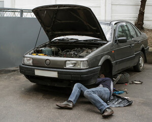 Car repair in urban garage as mechanic works beneath vehicle in late afternoon light
