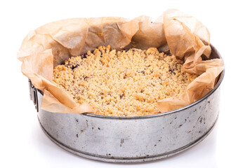 A freshly baked fruit pie with crumble topping in a round metal tin on a white background